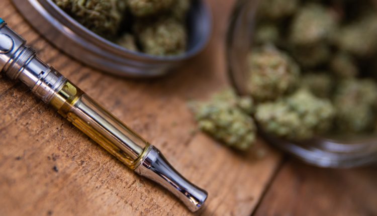 Cannabis Oil Vape Pen & Marijuana Buds In Open Glass Jar In Background